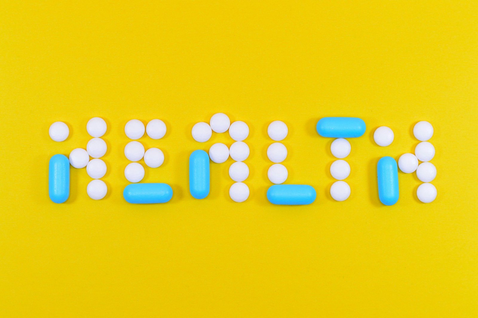 White and blue health pill and tablet letter cutout on yellow surface